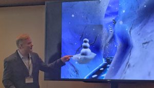 Photo pf a man pointing to a screen with an image of a virtual world called SnowWorld